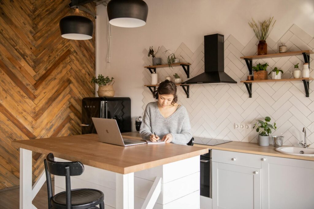 Busy female freelancer with laptop taking notes in kitchen